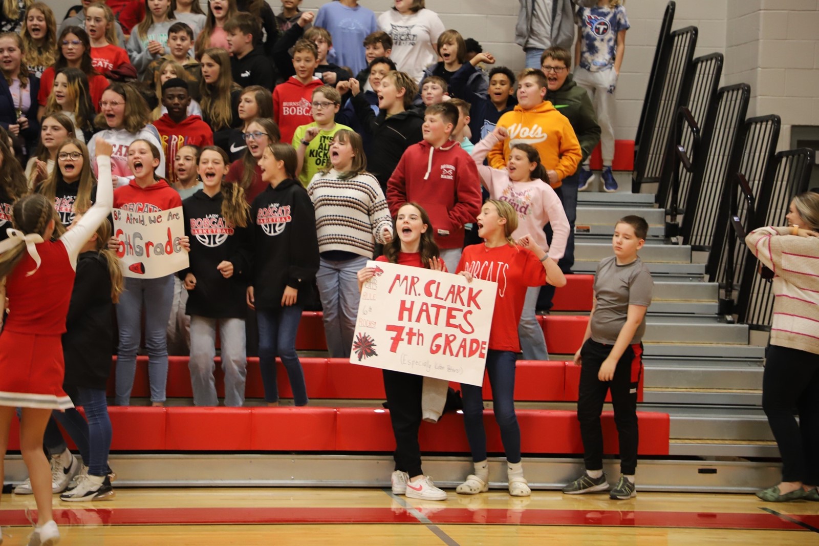 A crowd of students cheer in the stands of a school gym. 