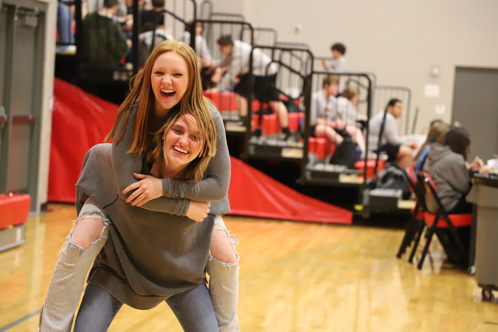 One student is on the back of another student in a school gym. 