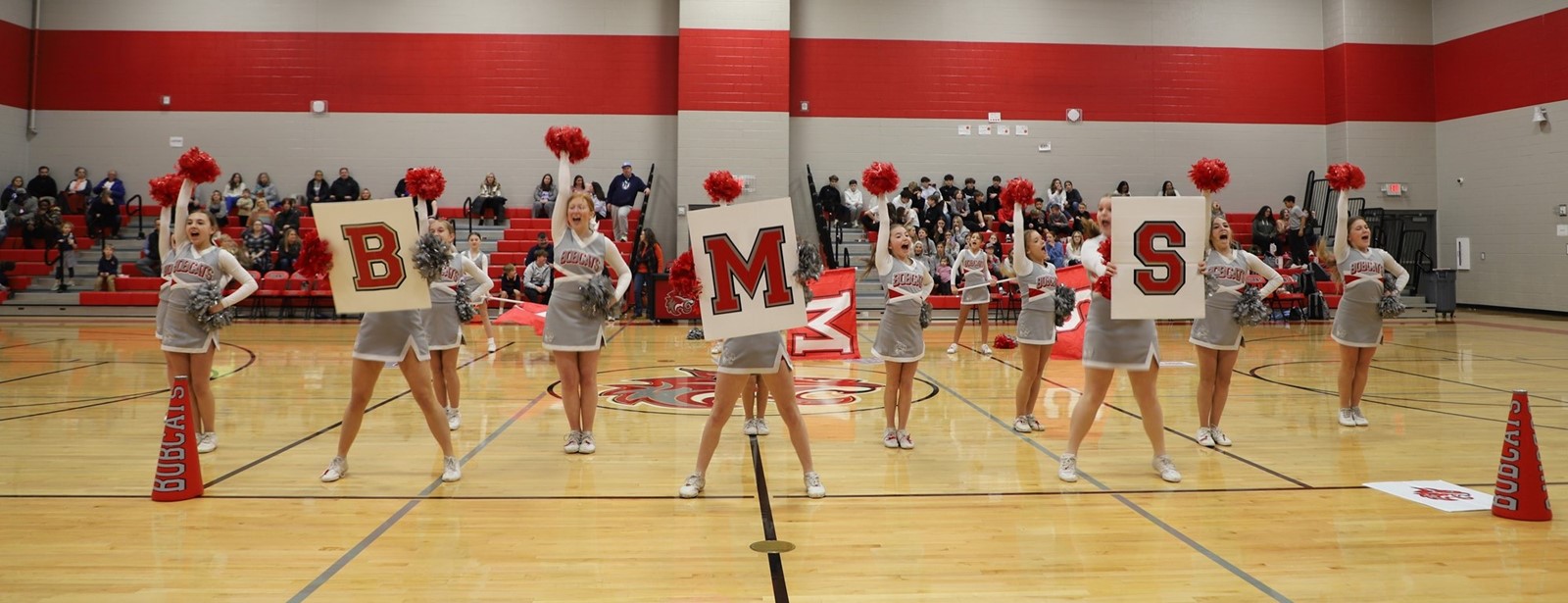 Cheer team holds up the letters B M S in the middle of a school gymnasium. 